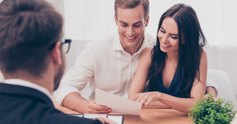 A young couple is looking over their auto insurance with a salesman in an office.