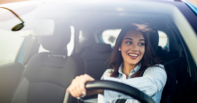 A smiling young businesswoman is inside her car with no passenger driving to work.