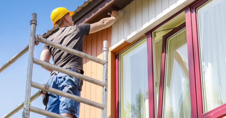 A man on scaffolding paints a home's exterior.