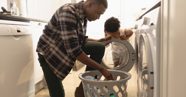 A man takes clothes out of the dryer while his son looks on