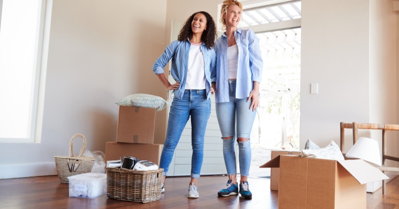 Two women are standing among boxes as they move into their new home.