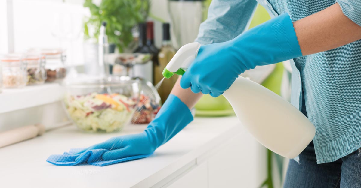 A woman from a cleaning service bends over a countertop and cleans it carefully, leading to a happy homeowner