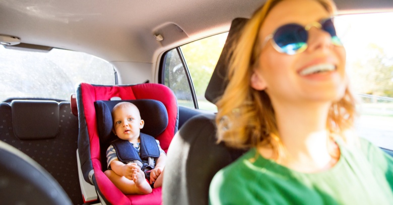 A woman is driving a car with her baby in the backseat. She is smiling because she was able to afford better car insurance after receiving her tax refund