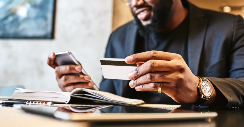 A man looks at his credit card and his phone as he prepares to put his tax refund towards paying down his credit card debt