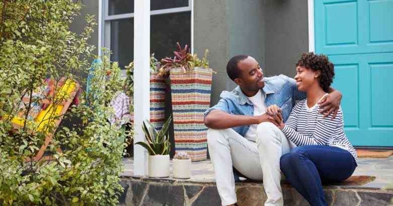 A young couple sits on the porch of their first home. They used tax refund money as their down payment.