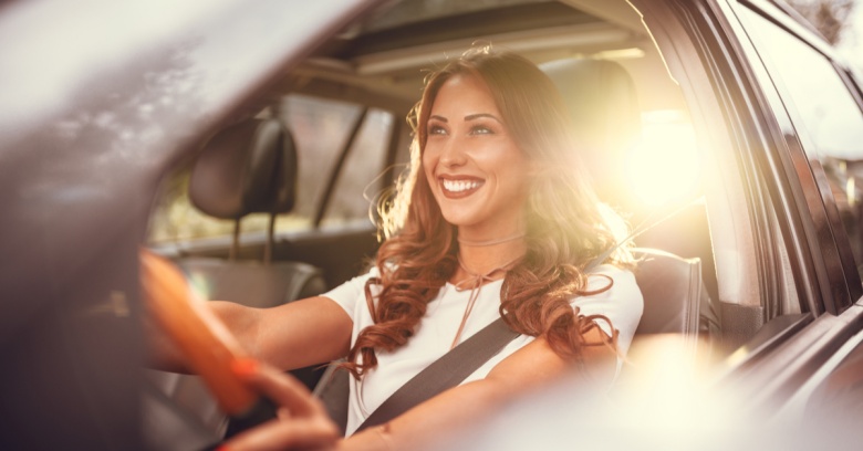 A woman drives with a smile on her face because she has just used her tax refund to pay off her car loan