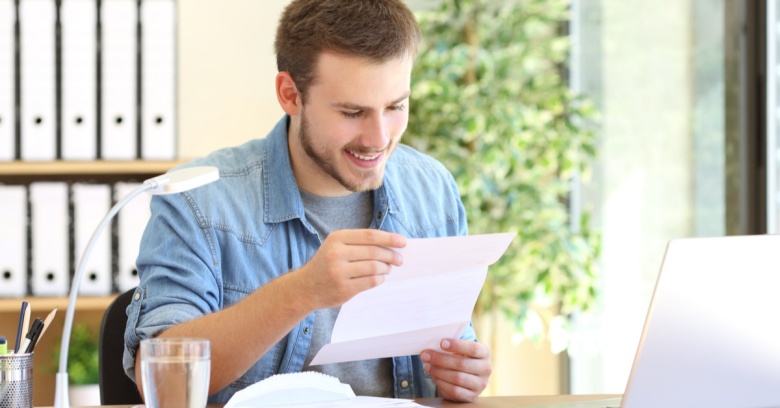 A young man reads a letter with a smile on his face. He is notified that he has paid off a debt.