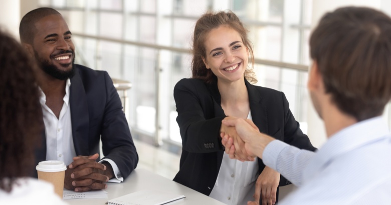 A young woman shakes the hand of a new employee. He will be starting a new job out of college.