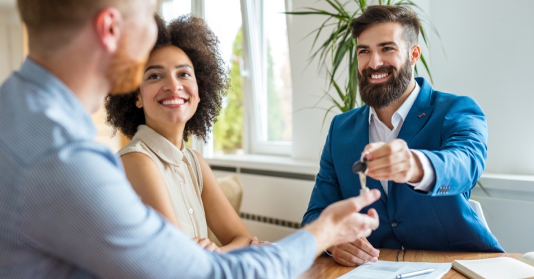 A young man and woman, both college graduates, are building their wealth by purchasing a home. They are receiving the keys to their new home from their real estate agent.