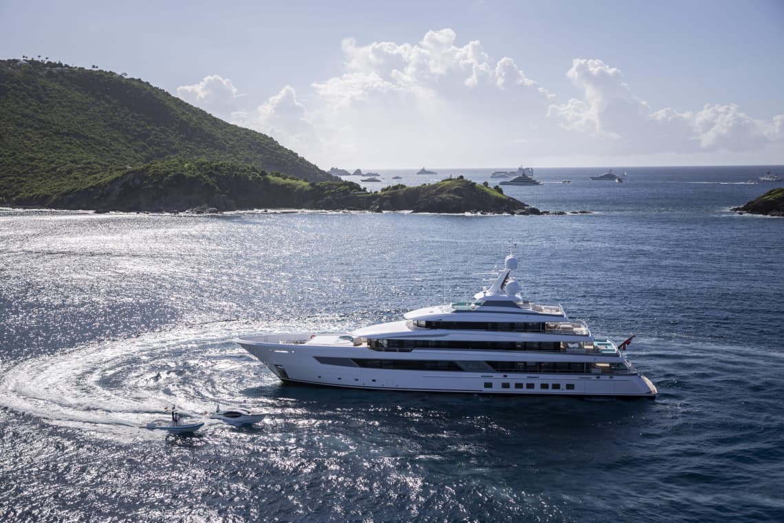 a yacht and 2 smaller boats in the water between 2 green mountains