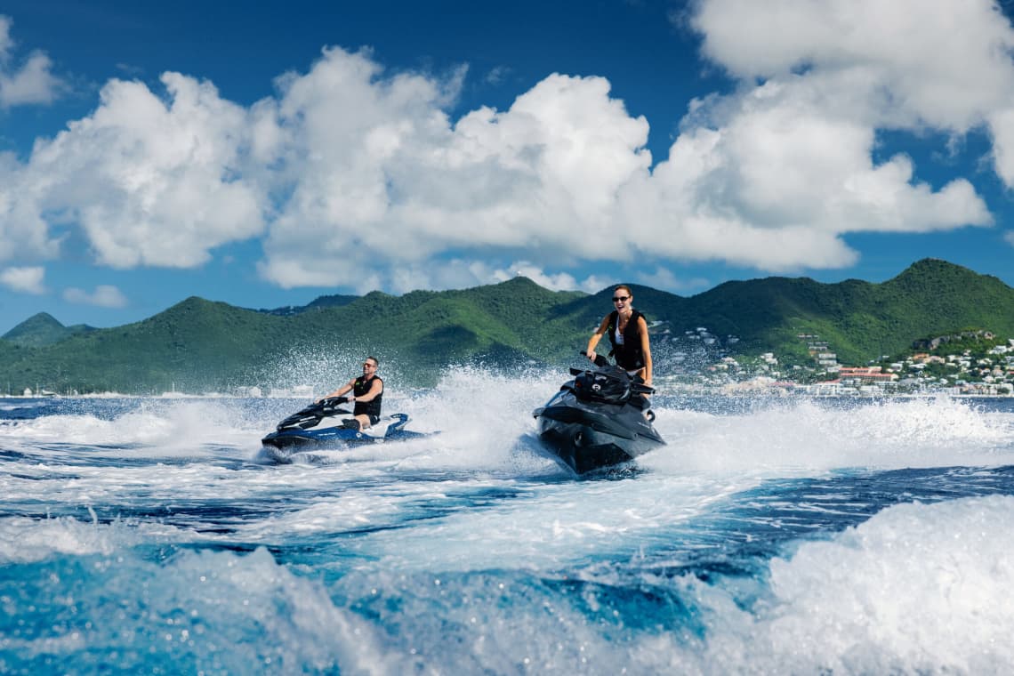 A Man and Woman Riding Jet Skis in the Water with Lush Green Mountains in the Background