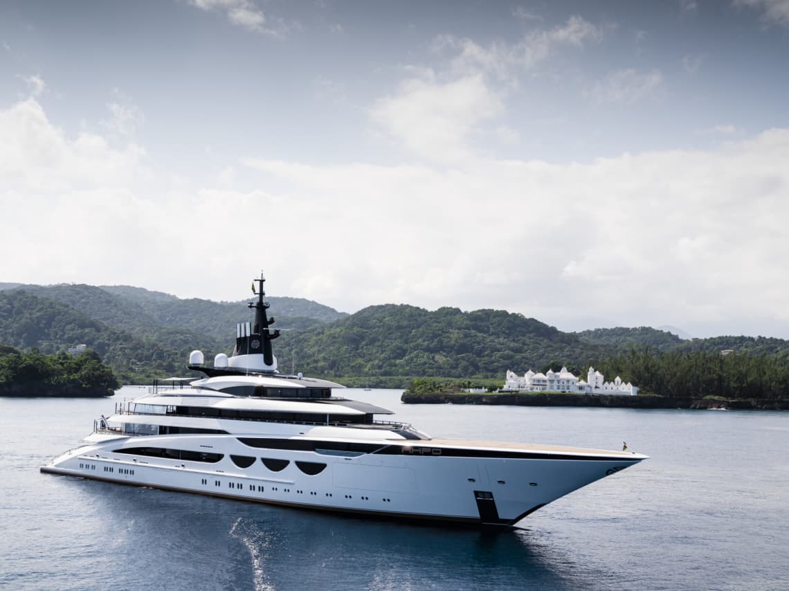Yacht on Open Water with Green Mountains in the Background and a Cloudy Sky