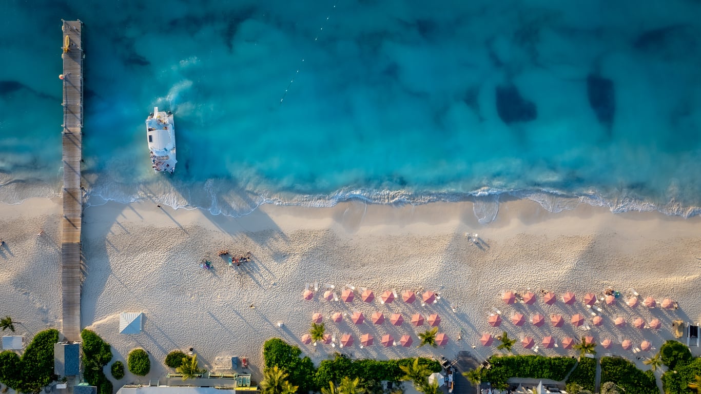 Drone image of sandy white beach with resort chairs and umbrellas in Turks and Caicos on Grace Bay. Ocean Club Resort is next to Club Med Beach dock.