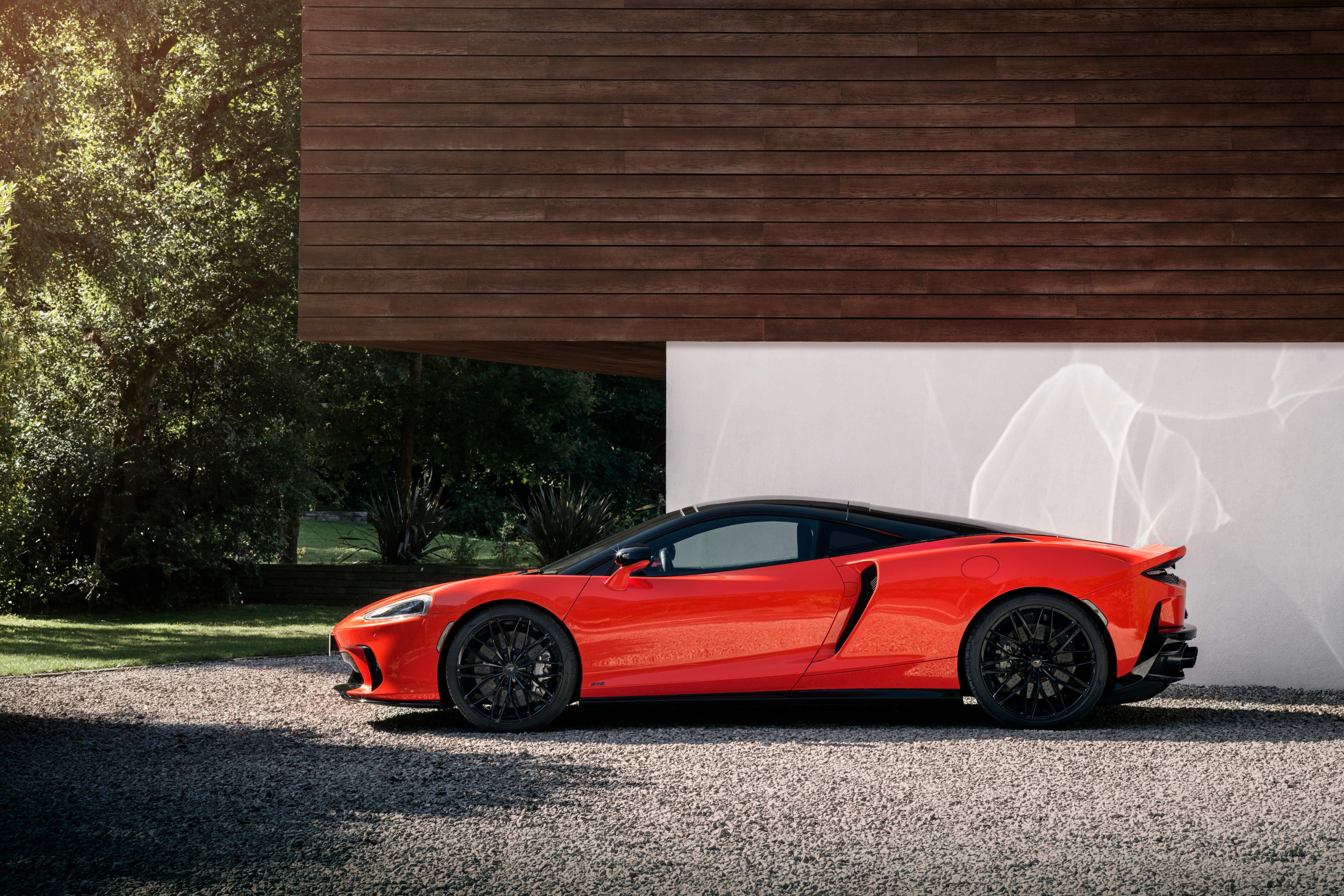 A dark grey McLaren GTS parked in the shade of a concrete underpass, front three-quarter view
