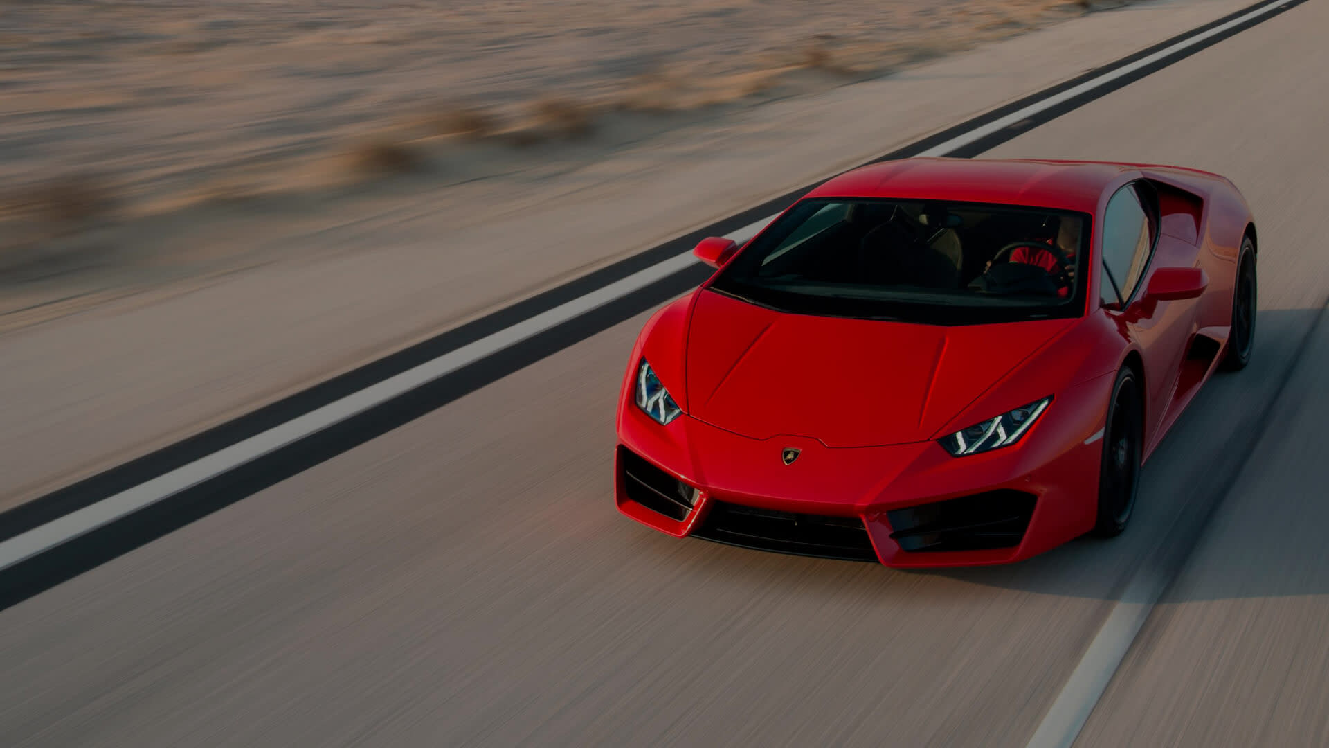 Front three-quarter view of a Lamborghini Huracán RWD driving on a dry mountain road, highlighting its angular front design and signature LED lights