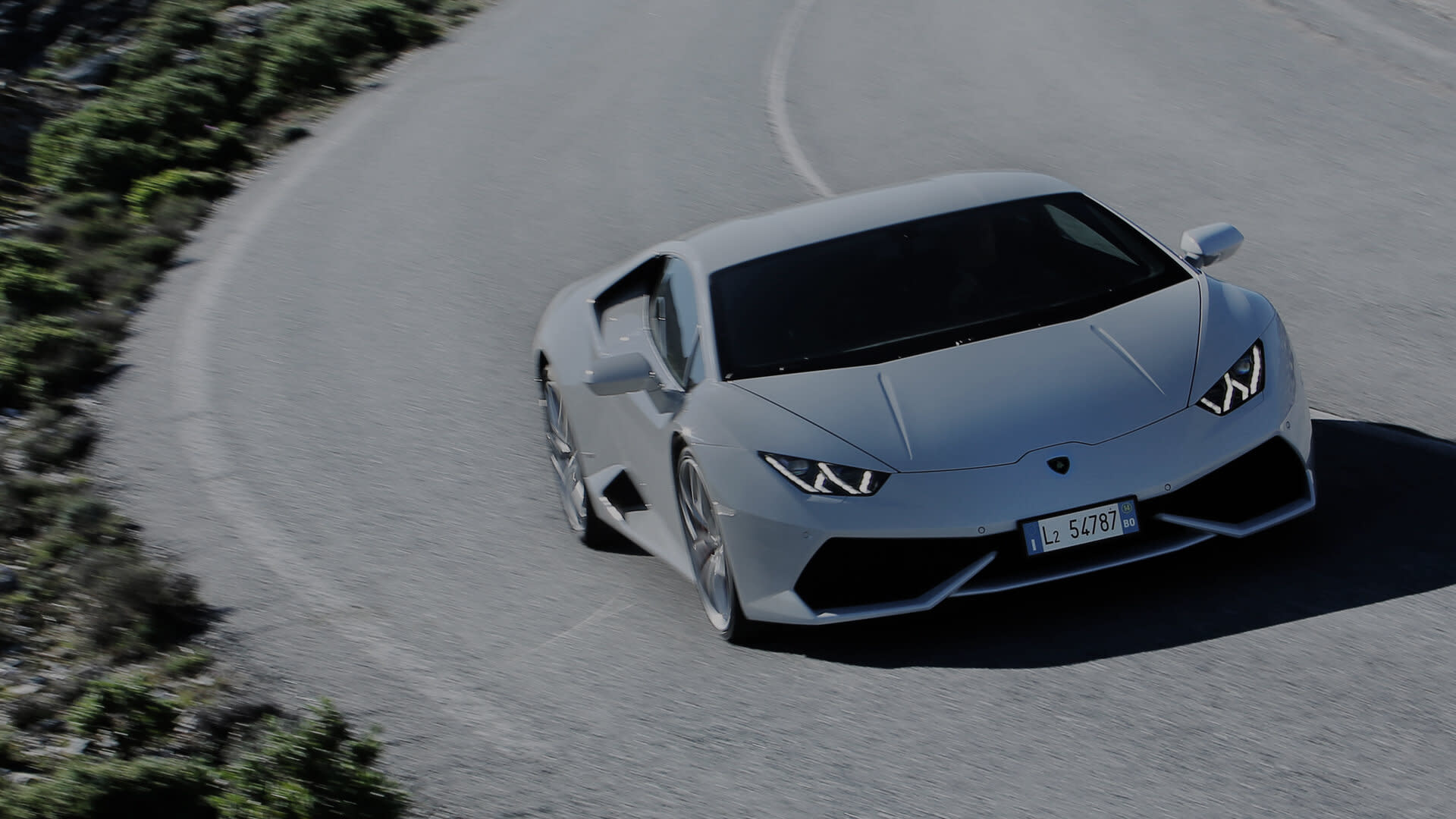 Front angle of a white Lamborghini Huracán Coupé parked on a coastal road with the ocean in the background