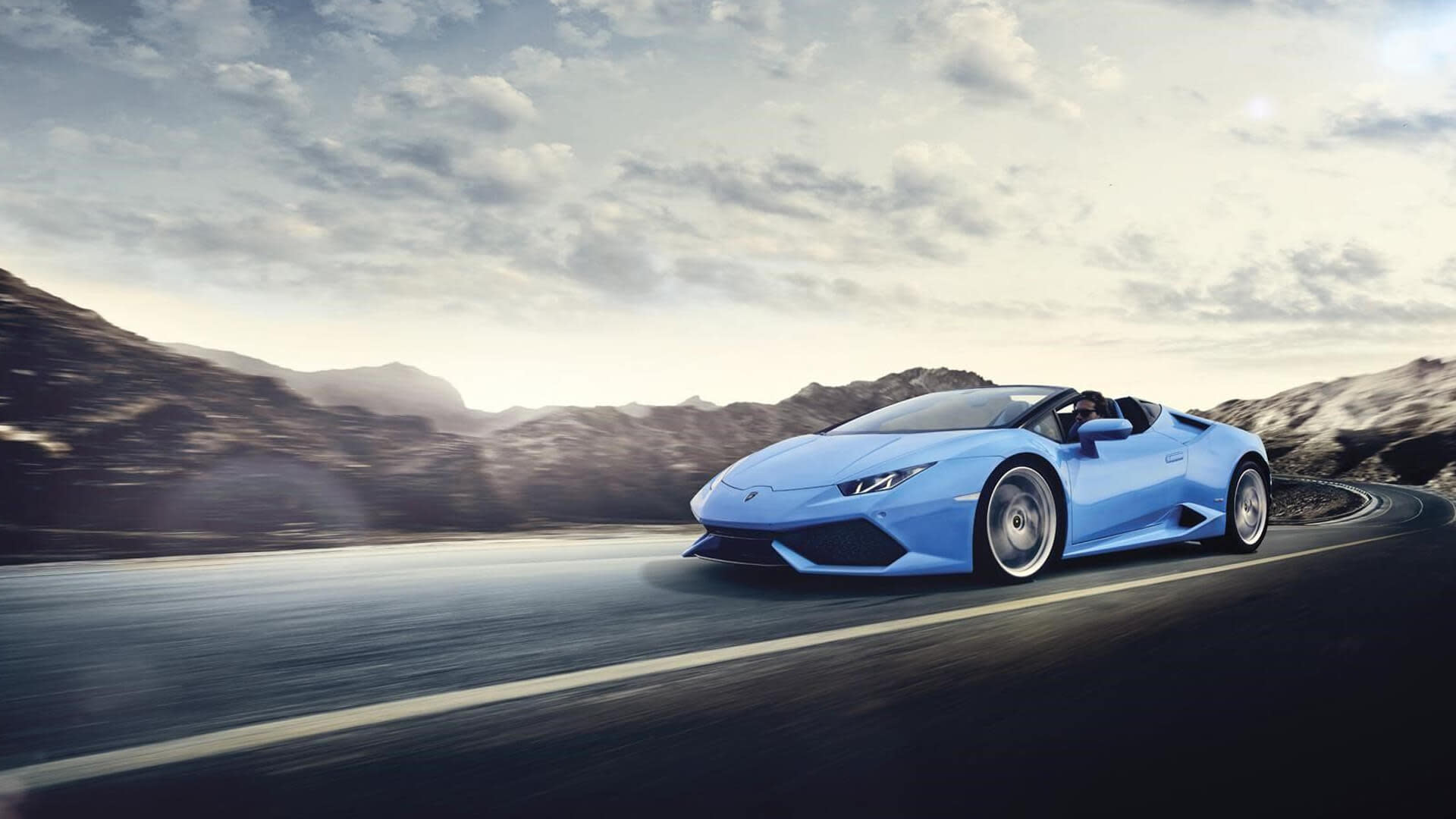 Lamborghini Huracán Spyder ярко-желтого цвета едет по прибрежной дороге с опущенной крышей, подчеркивая ощущение езды на открытом воздухе