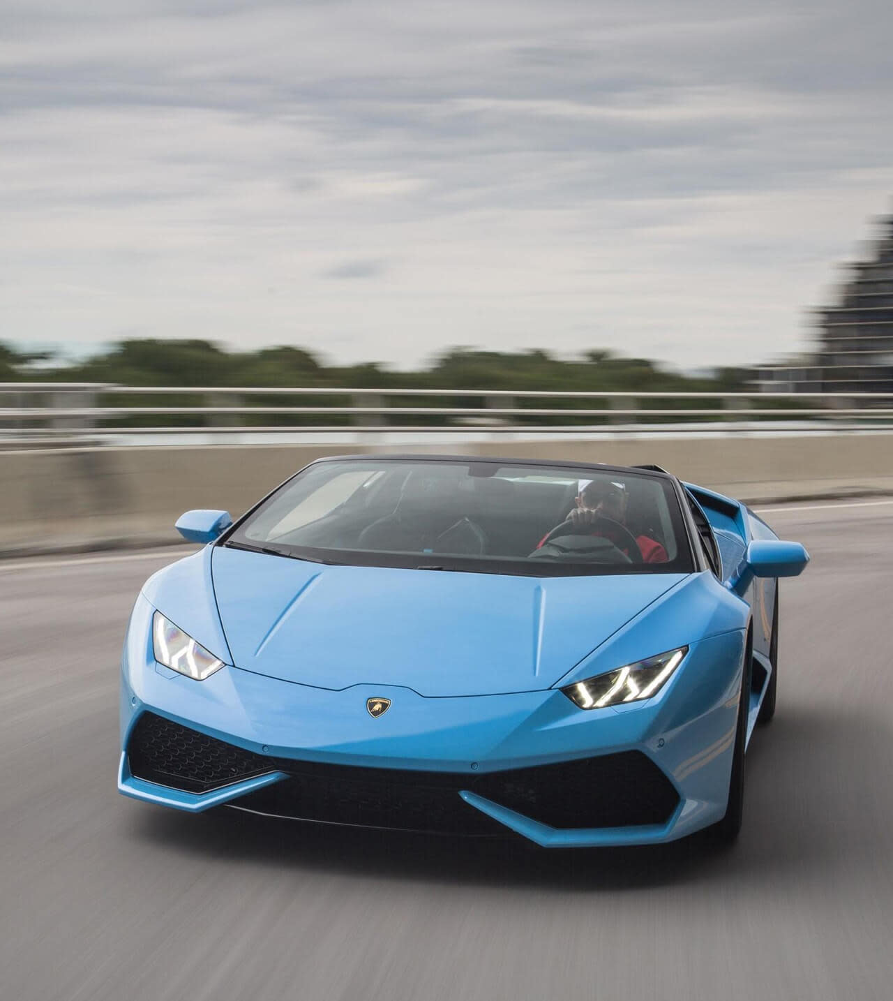 Вид сбоку на подержанный Lamborghini Huracán Spyder в городских условиях с опущенным верхом, демонстрирующий элегантный дизайн