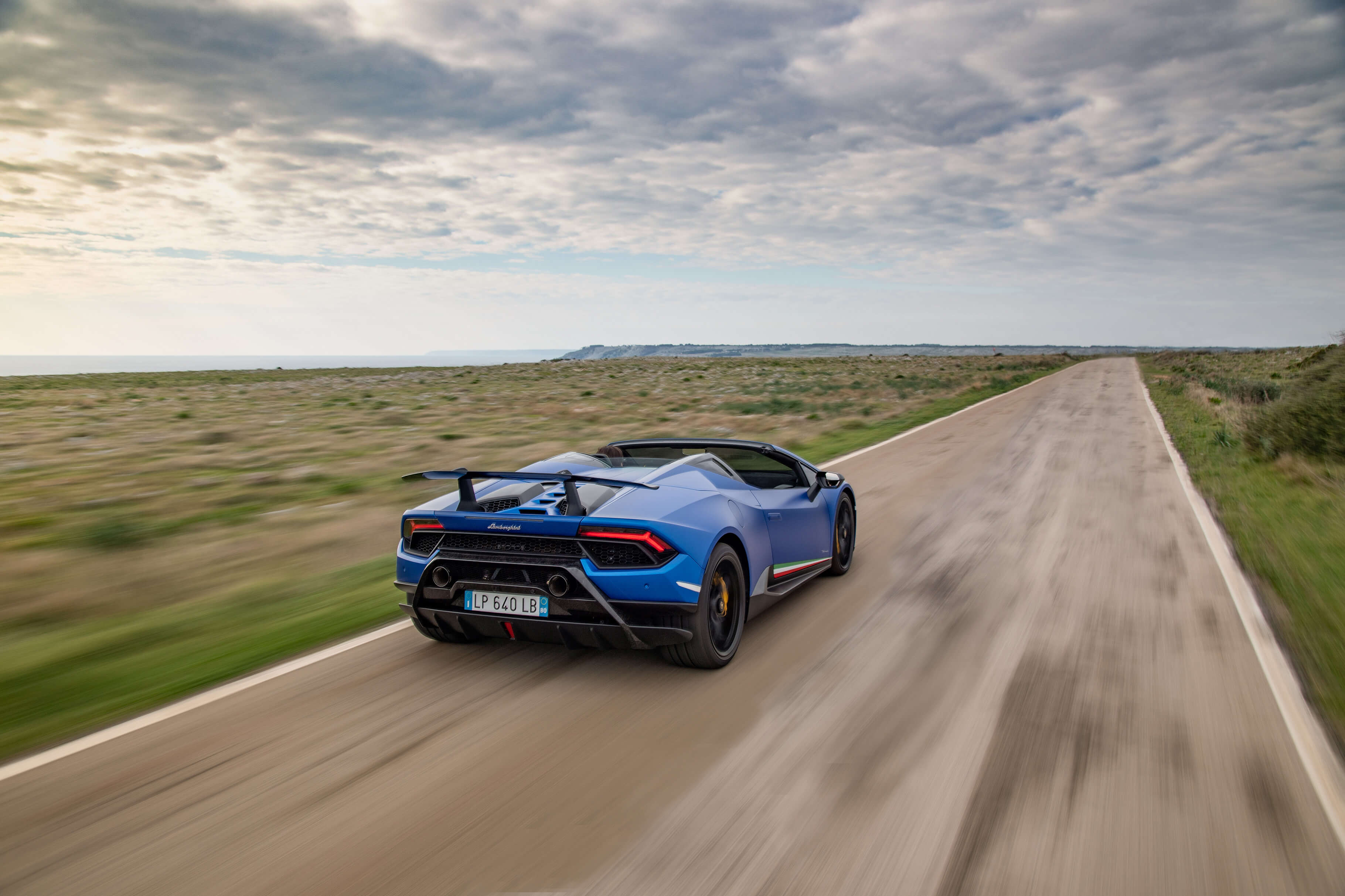 Lamborghini Huracán Performante Spyder in Bewegung auf der Strecke mit offenem Verdeck, Rückperspektive mit hervorgehobenem aerodynamischen Heckflügel und Diffusor