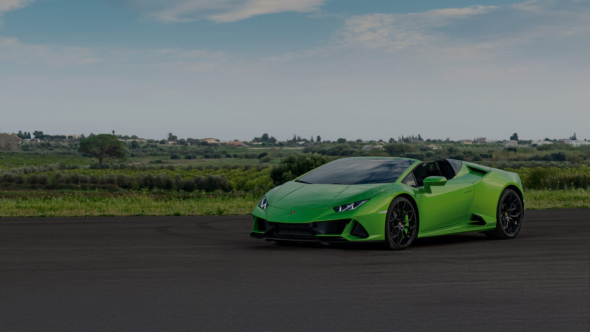 Front three-quarter view of a Lamborghini Huracán EVO Spyder with the top down, driving along a mountain road on a sunny day