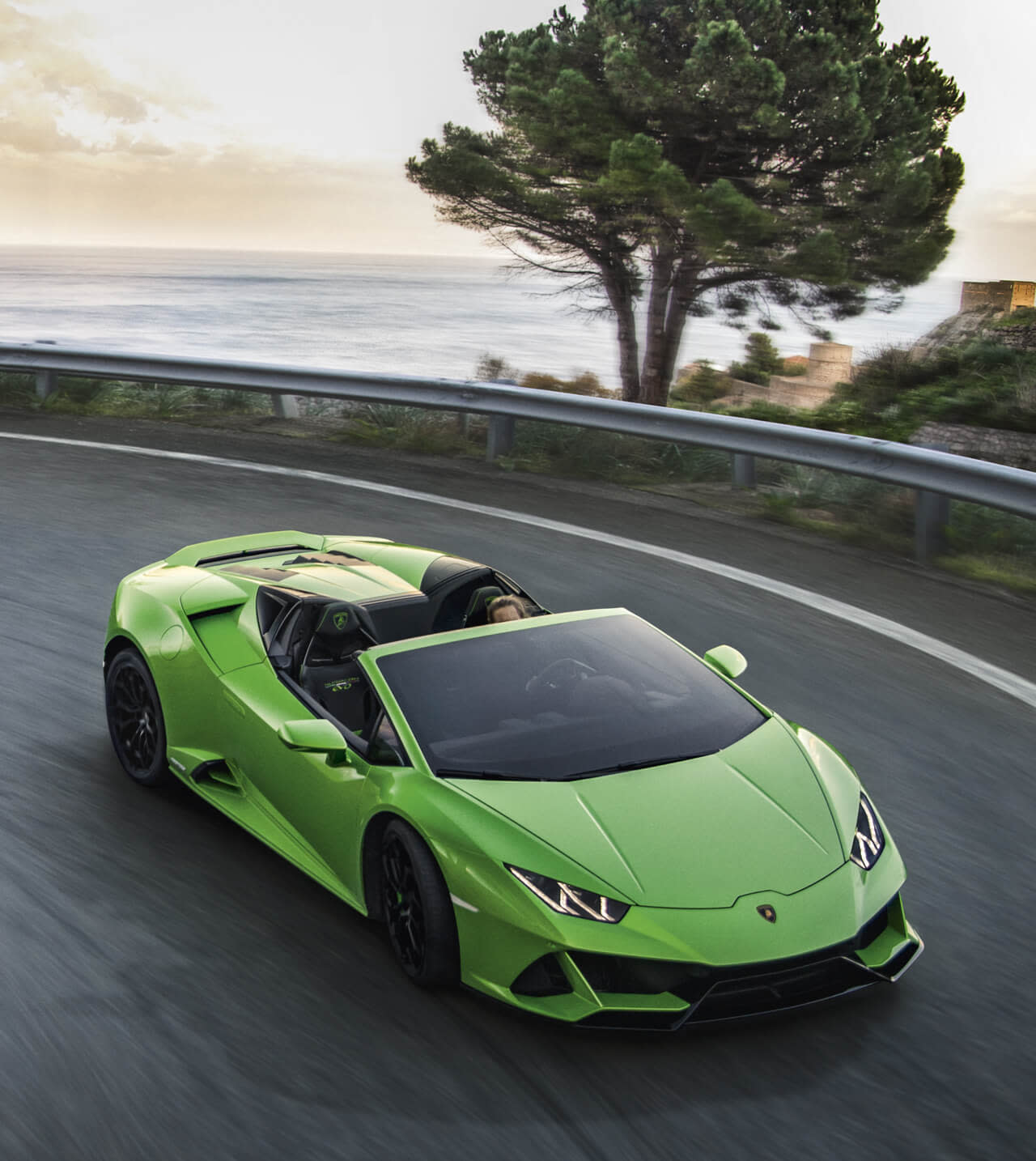 Side view of a Lamborghini Huracán EVO Spyder parked on an open road with dramatic hills in the background