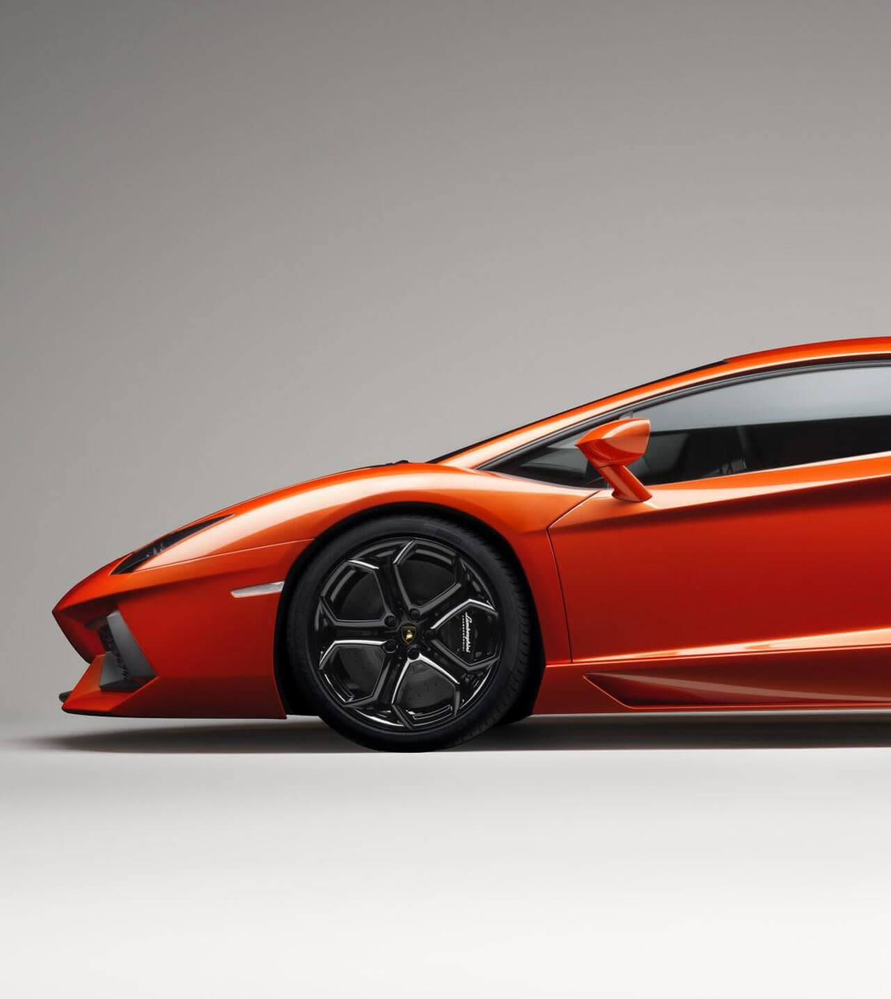 Vista trasera de un Lamborghini Aventador Coupé naranja estacionado de noche frente al Castillo Sant'Angelo en Roma, iluminado por las luces de la calle.