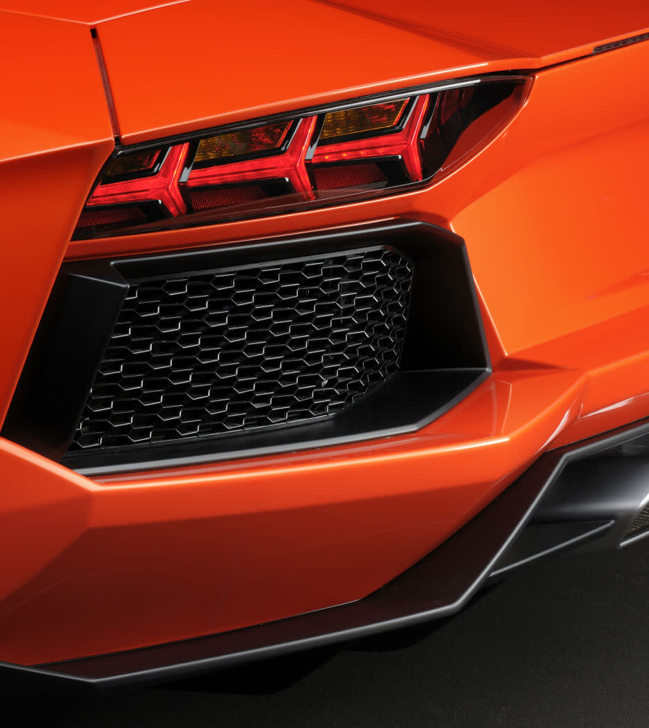 Perfil lateral de un Lamborghini Aventador coupé naranja sobre un fondo gris neutro.