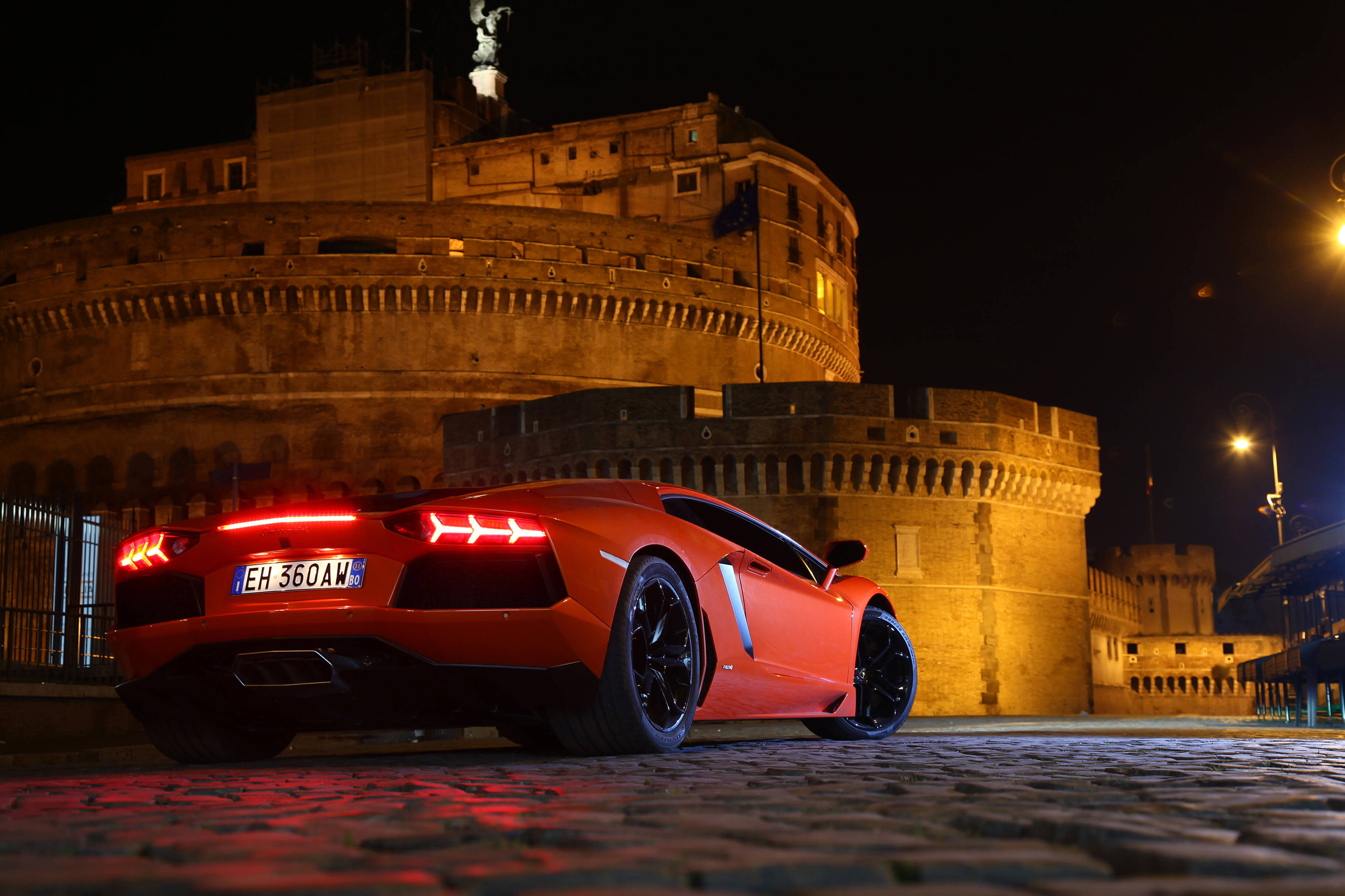 Ángulo trasero de un Lamborghini Aventador Coupé circulando por una carretera de montaña al atardecer