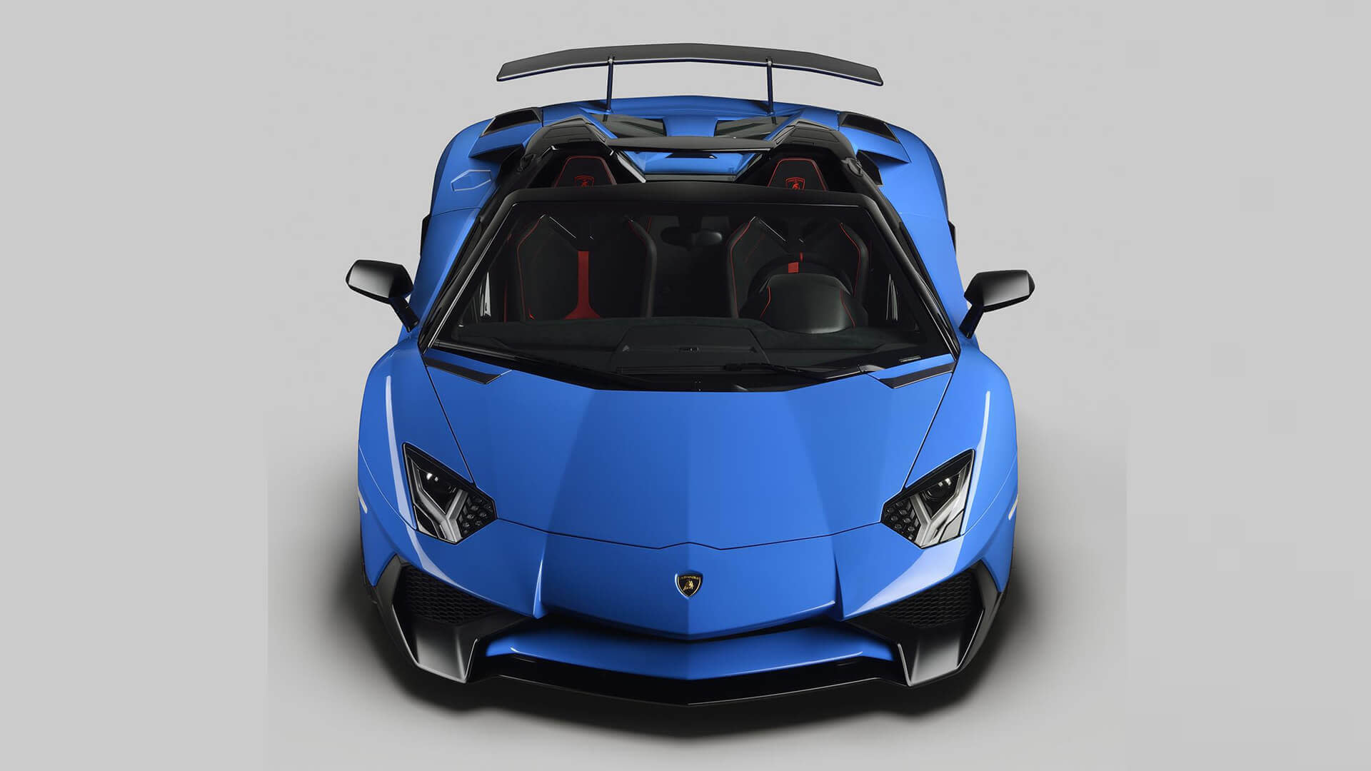 Rear angle of a red Lamborghini Aventador Superveloce Roadster driving on a racetrack during sunset.