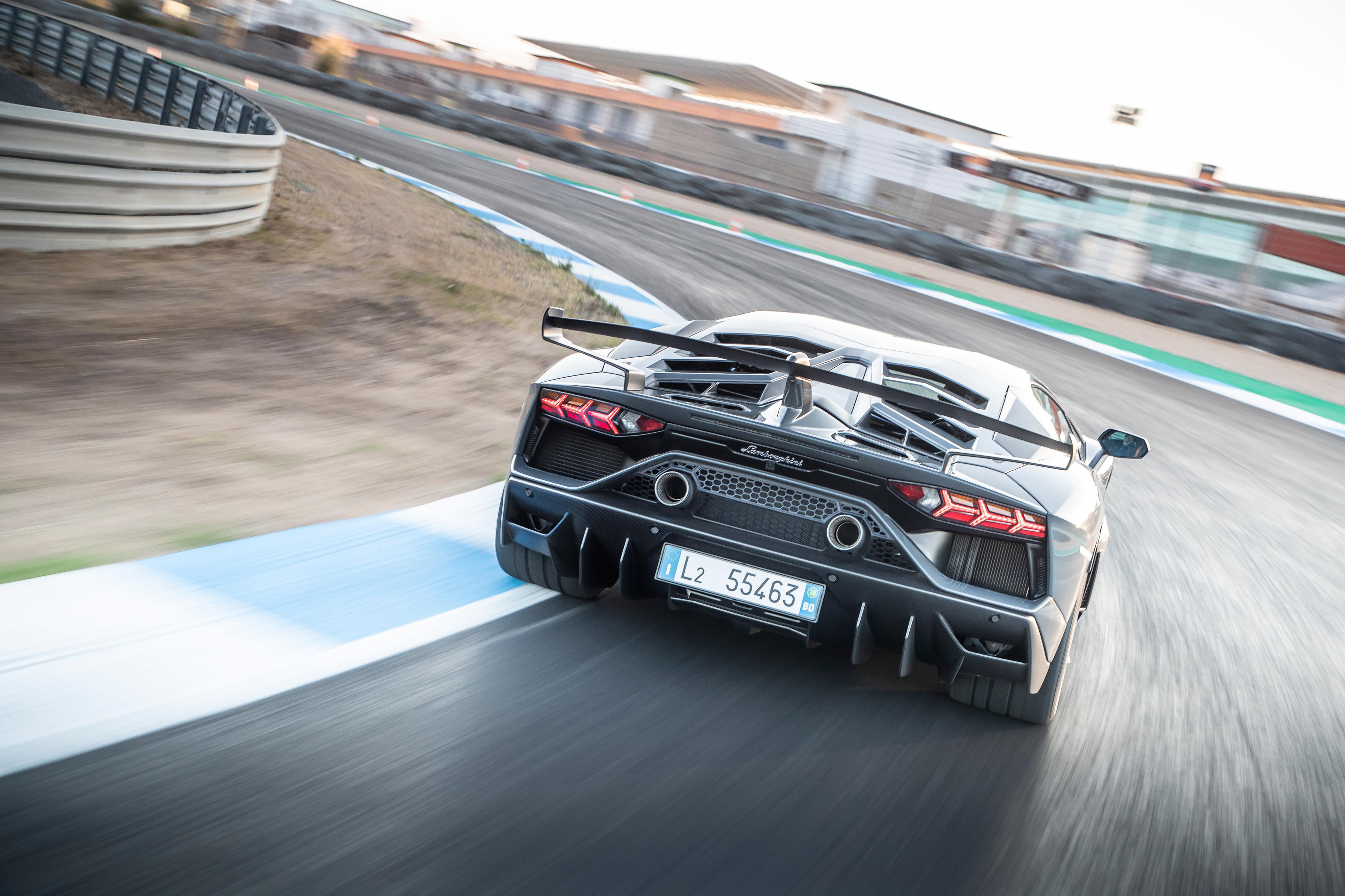 Rear angle of a Lamborghini Aventador SVJ accelerating on a closed racetrack at sunset.