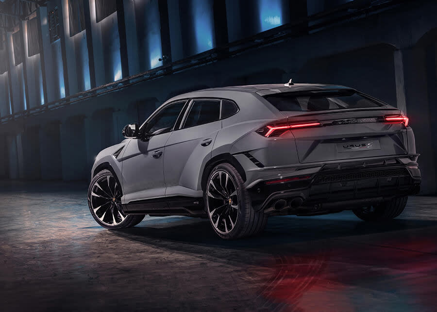 Side profile of a Lamborghini Urus S driving on a coastal road with cliffs in the background