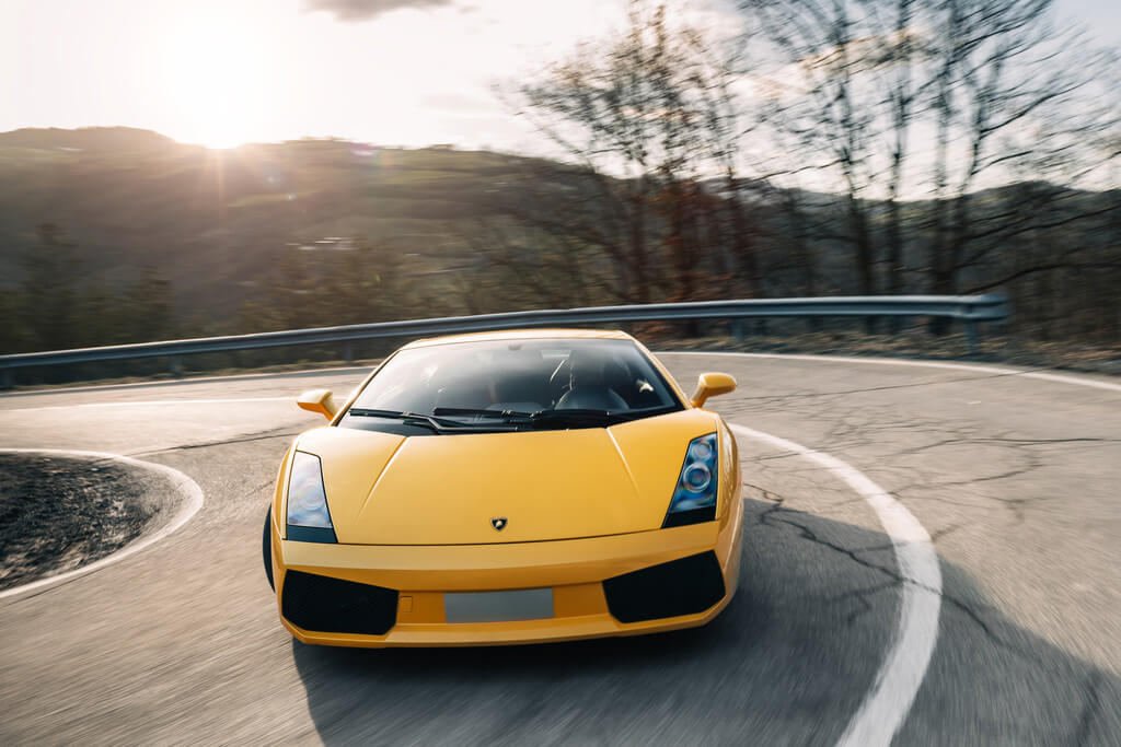 La parte anteriore di una Lamborghini Gallardo che percorre una strada fiancheggiata da alberi