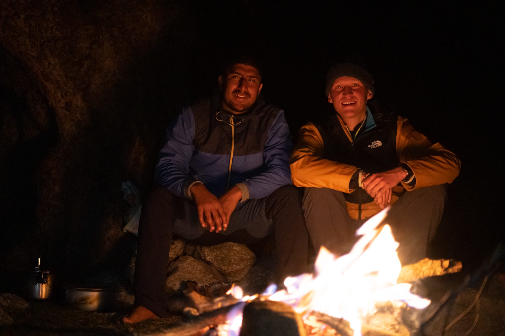 2 people sitting in the dark behind a fire