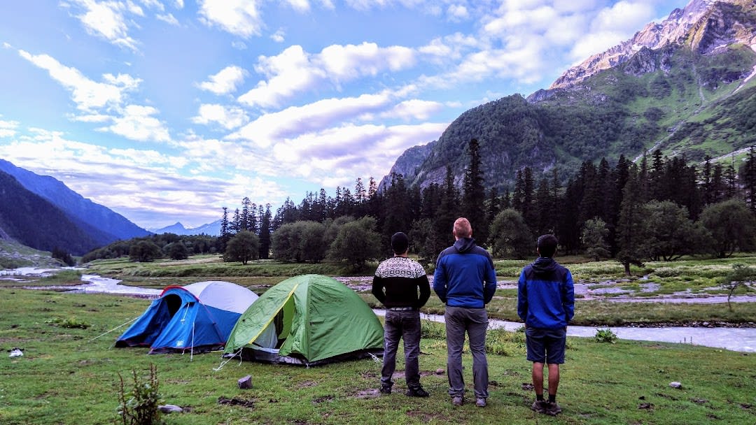 3 man standing right next to 2 tents, looking at the mountains