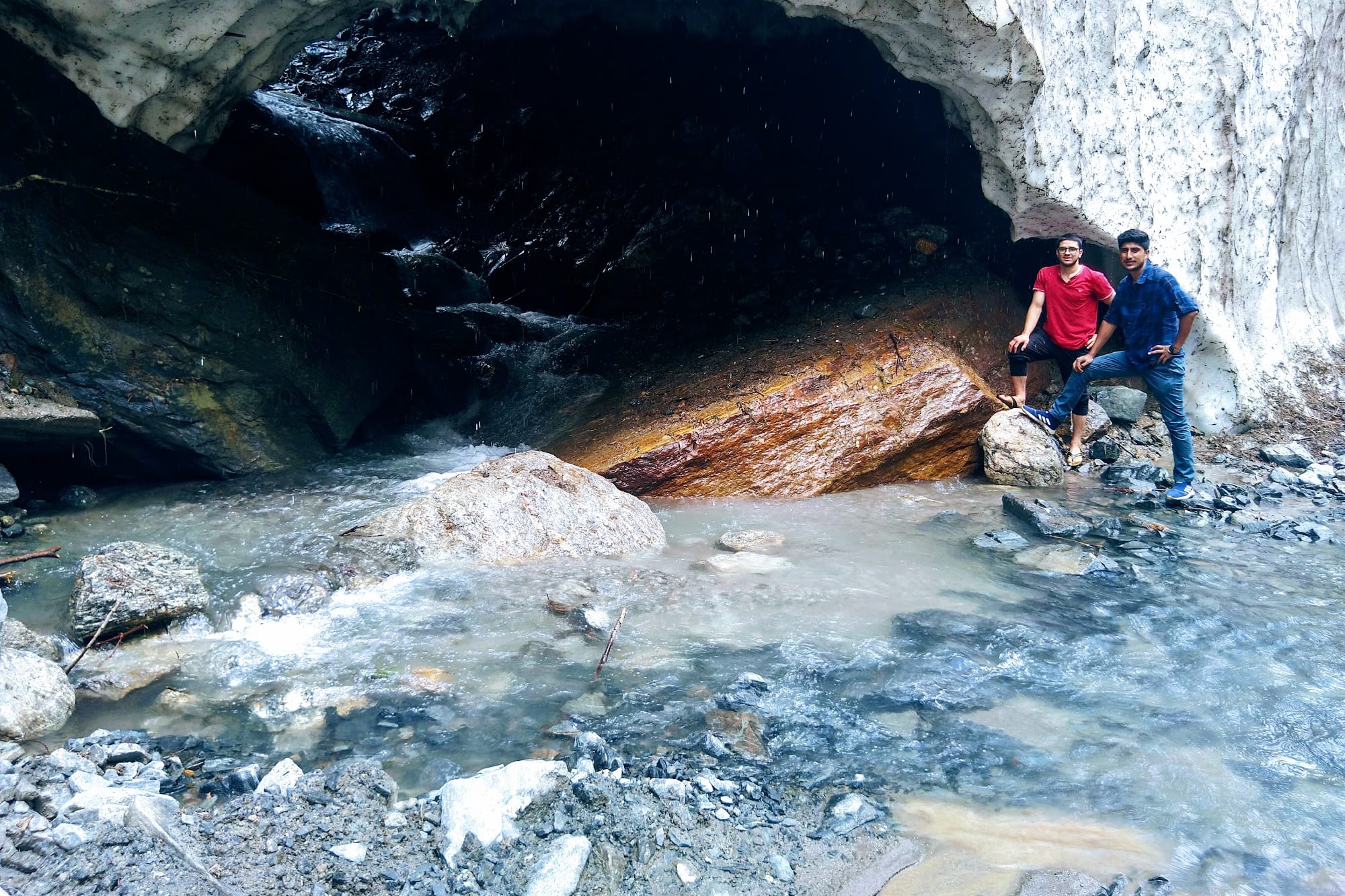 2 people inside an snow cave with the river flowing through it