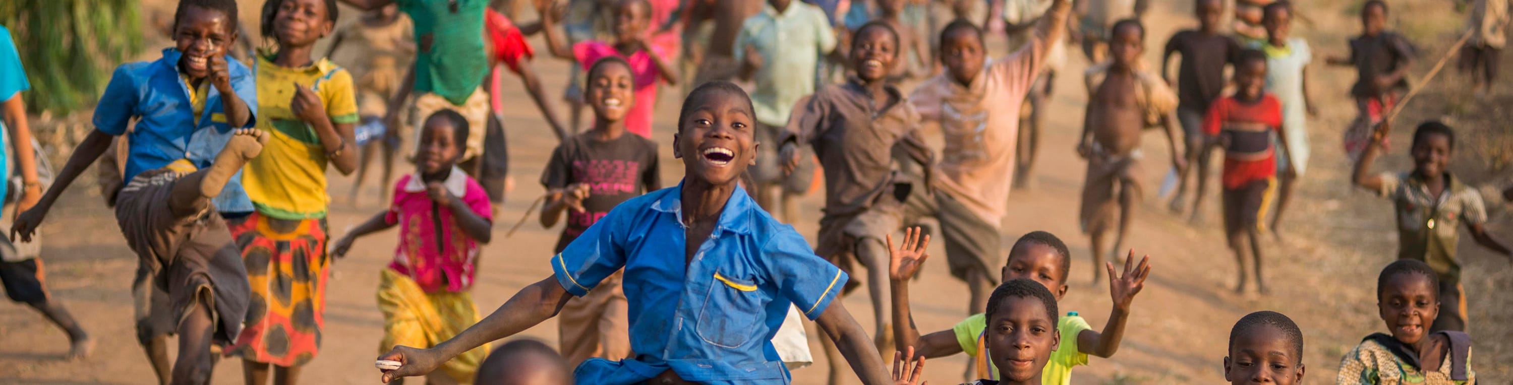 Happy African children running down a street. Two boys in the foreground are jumping
