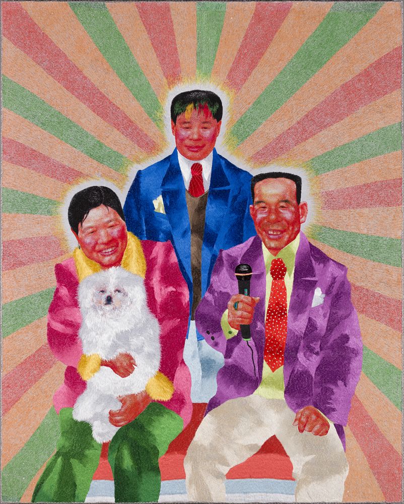 Embroidery on cotton depicting three people with coloured rays emanating from them. A woman holding a Pomeranian is on the left, seated beside a man with a microphone. A man stands behind them.