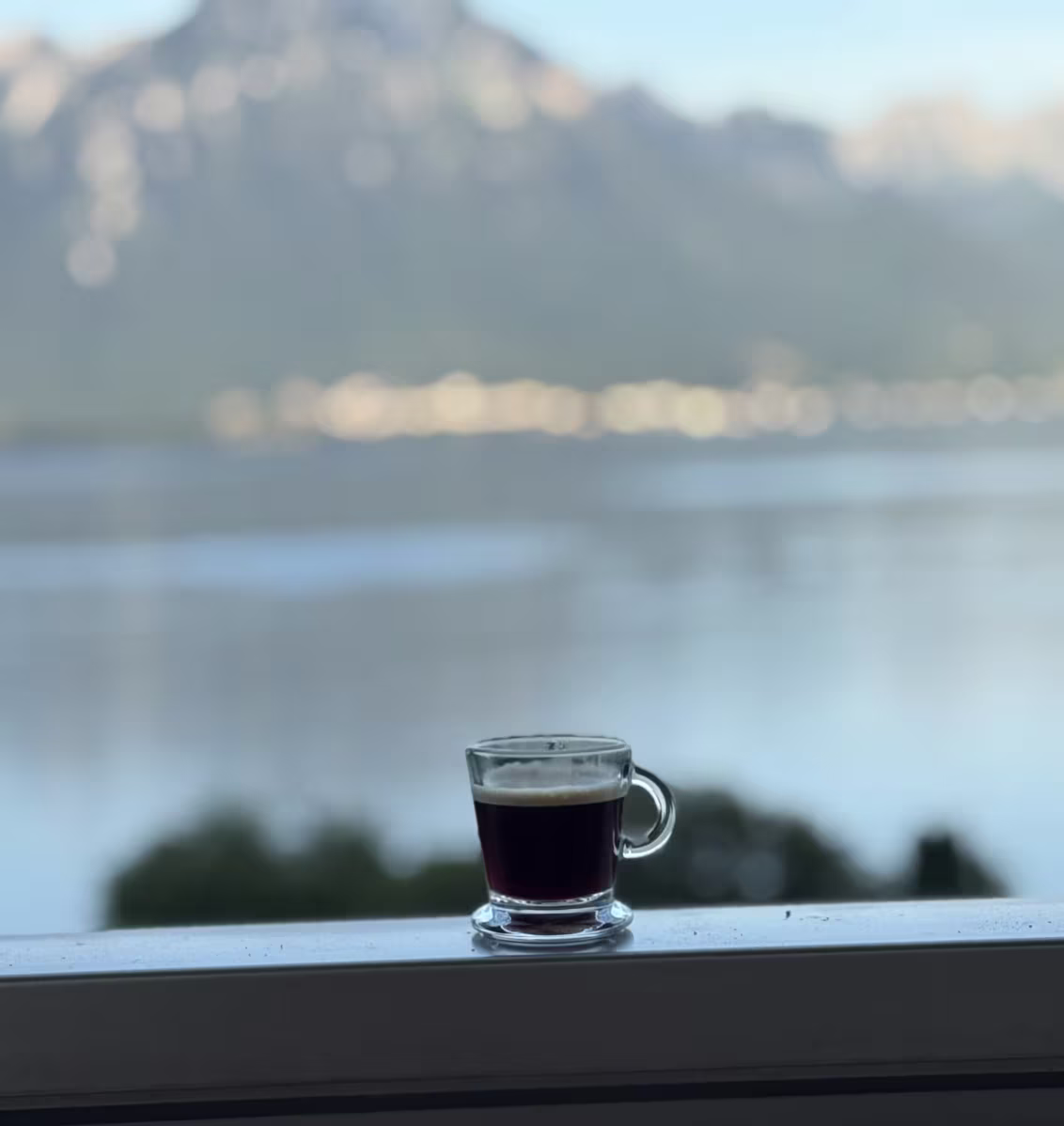 Image of cup of coffee set on top of balcony with Lake Geneva and Alps in background