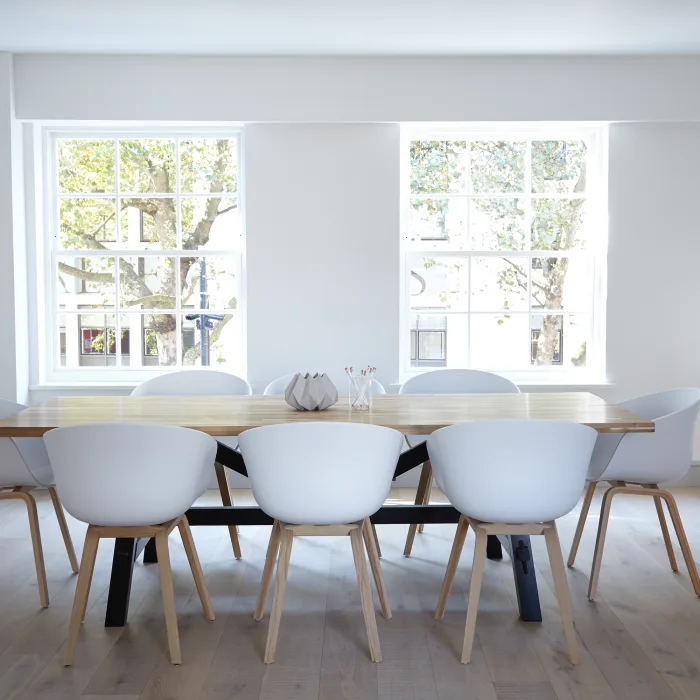 Uma sala clara e bem iluminada com uma mesa ao centro e algumas cadeiras modernas.