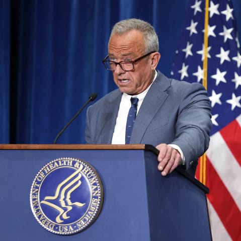 Robert F. Kennedy Jr. speaks into a microphone behind a podium with insignia for the Department of Health and Human Services.