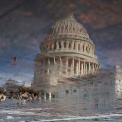 The Capitol is reflected in a puddle.