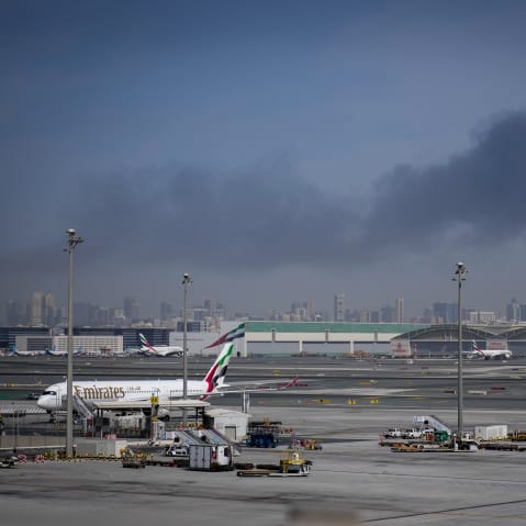 An airplane is parked at an airport with smoke seen in the background.