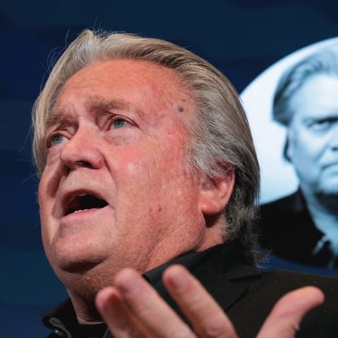 Steve Bannon speaks as he makes a hand gestures. In this very tight portrait that was shot from below, you can see another portrait of him in the background.