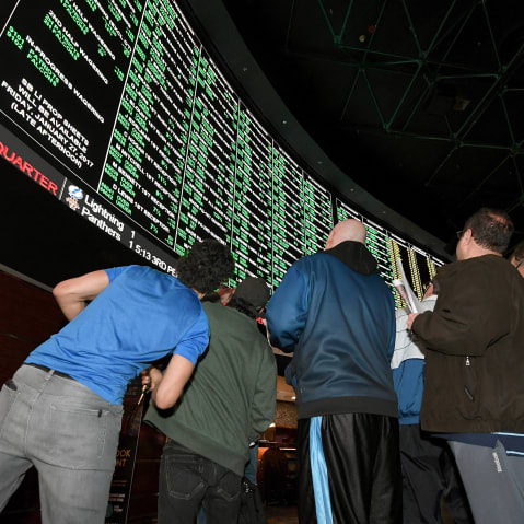 People look up toward a betting odds video board.