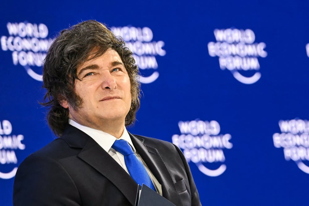 Javier Milei looks up in front of a background that repeats "World Economic Forum."