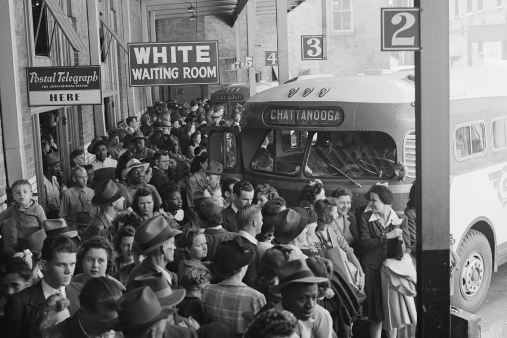A black-and-white photo from 1943 showing a crowded bus terminal with a hanging sign that reads "White Waiting Room."