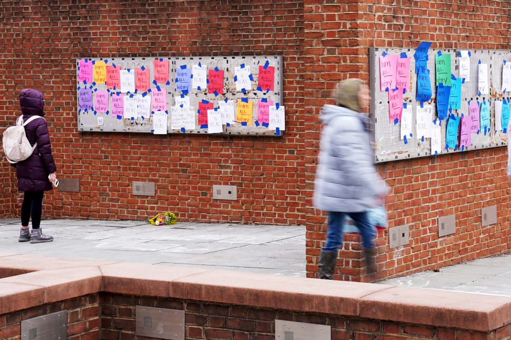 One person looks at posted signs while two others walk by explanatory panels that were part of an exhibit on slavery at President's House Site.
