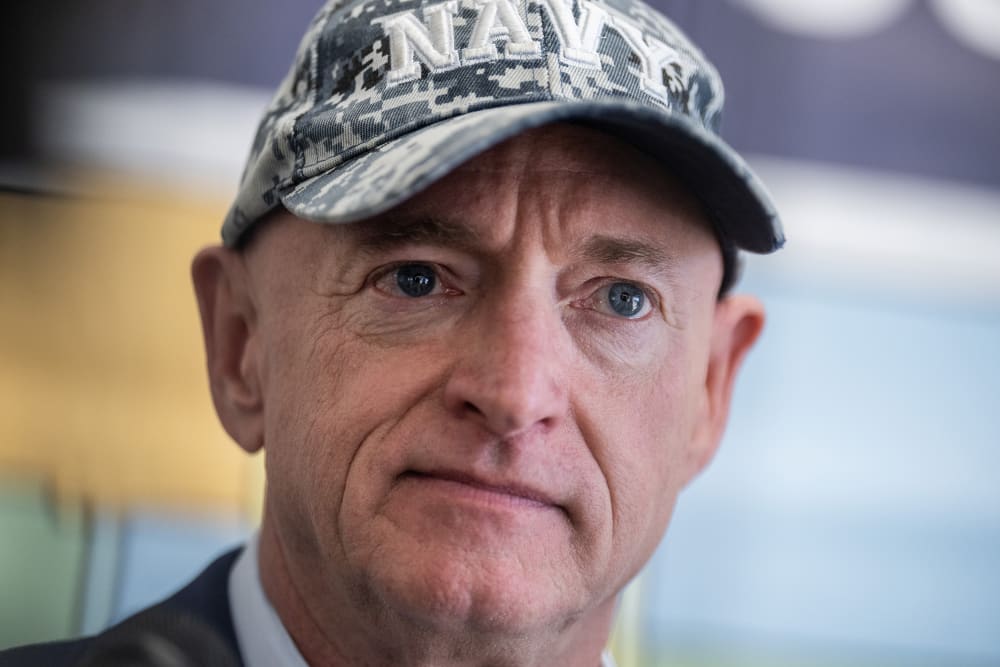 Arizona Sen. Mark Kelly looks on at an event, wearing a Navy cap.