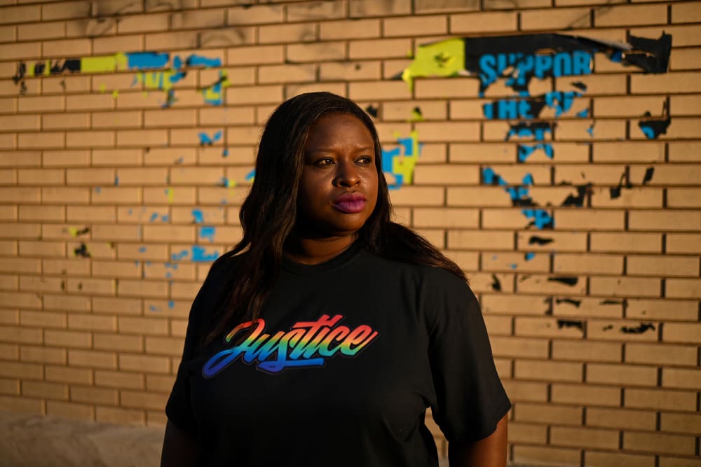 Nekima Levy Armstrong, wearing a shirt that says "justice" in rainbow letters, poses in front of a brick wall.