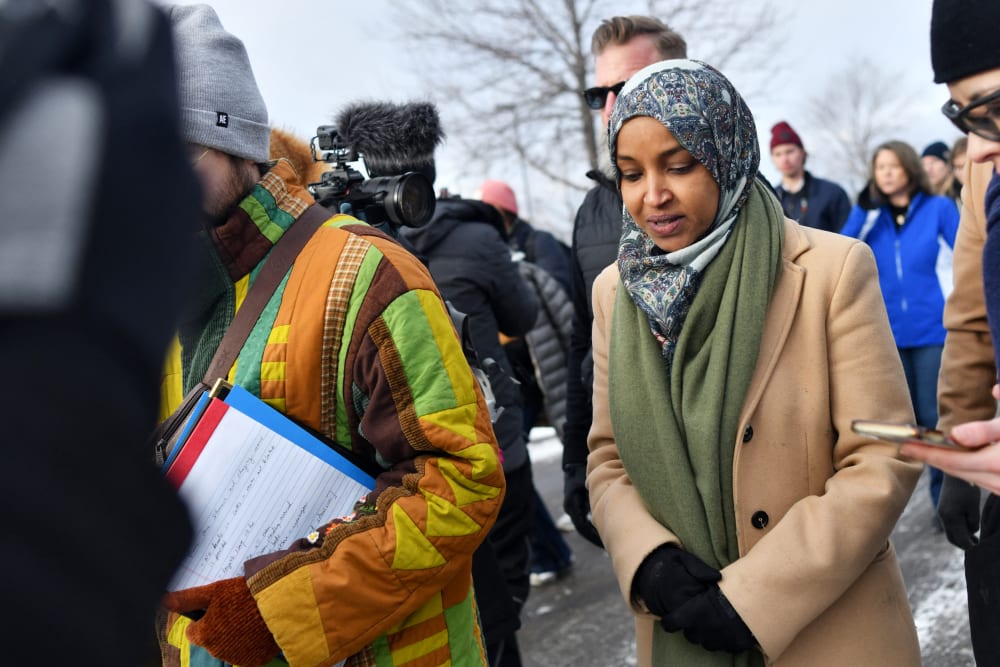 Ilhan Omar talks to a reporter as she walks on the street in winter.